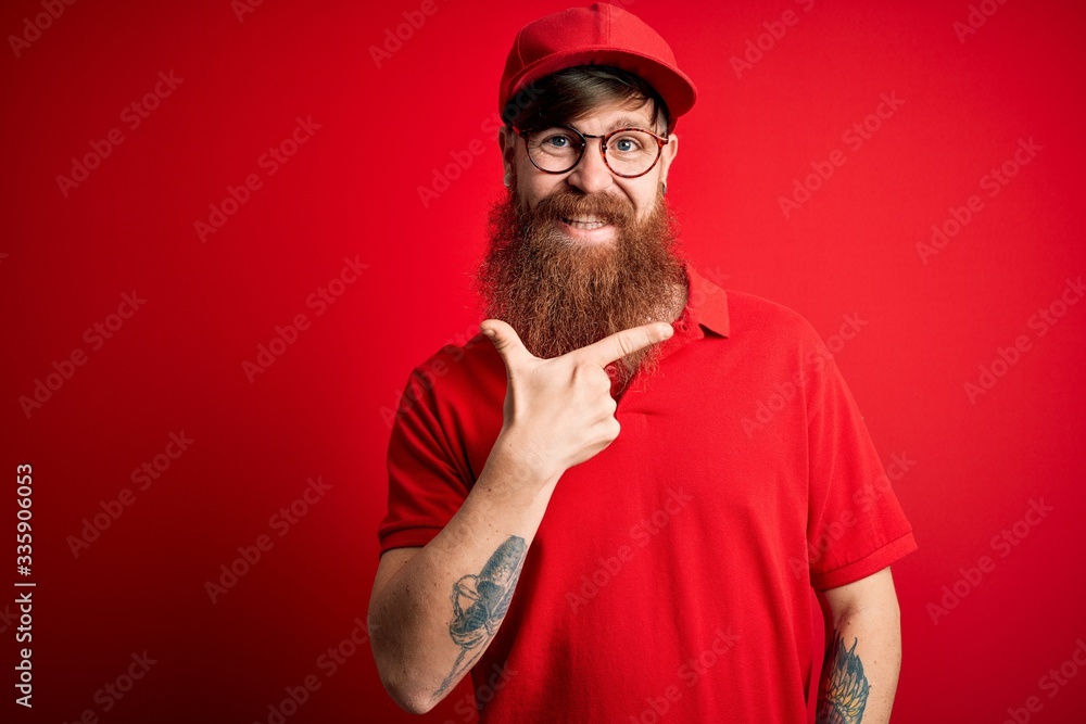 Young handsome delivery man wearing glasses and red cap over isolated background cheerful with a smile on face pointing with hand and finger up to the side with happy and natural expression Young handsome delivery man wearing glasses and red cap over isolated background cheerful with a smile on face pointing with hand and finger up to the side with happy and natural expression