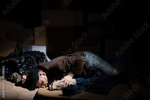 A homeless middle-aged man sleeps in cardboard boxes outside. © fotodrobik