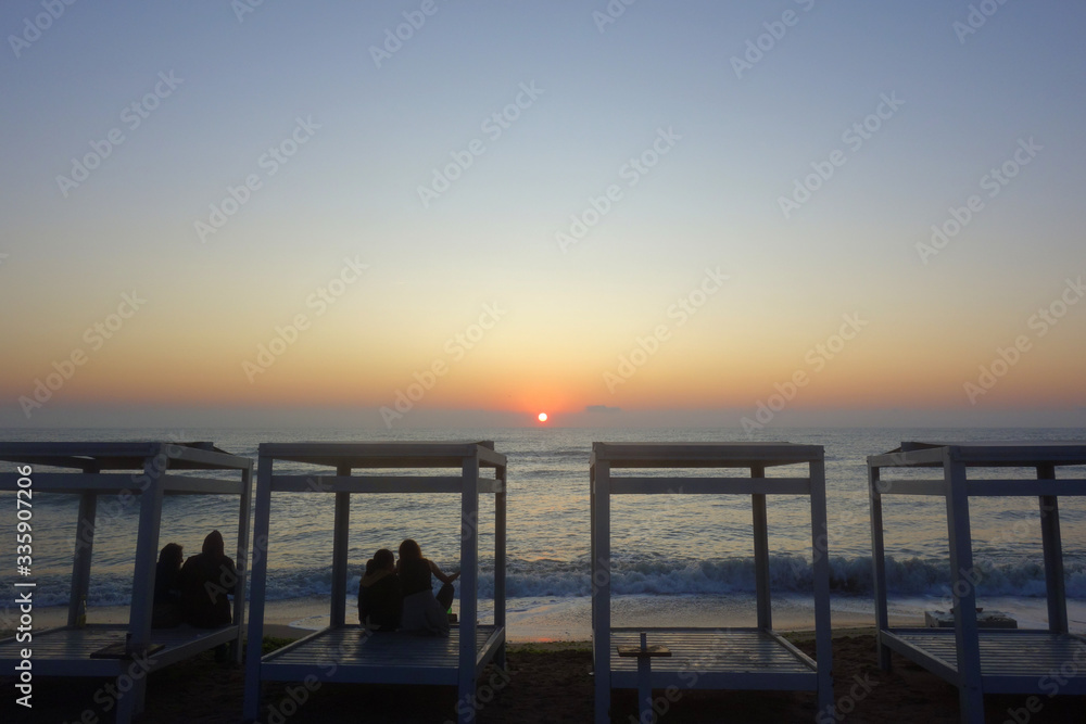 Young people on seashore watching the sun rise in Vama Veche at the Black Sea in Romania