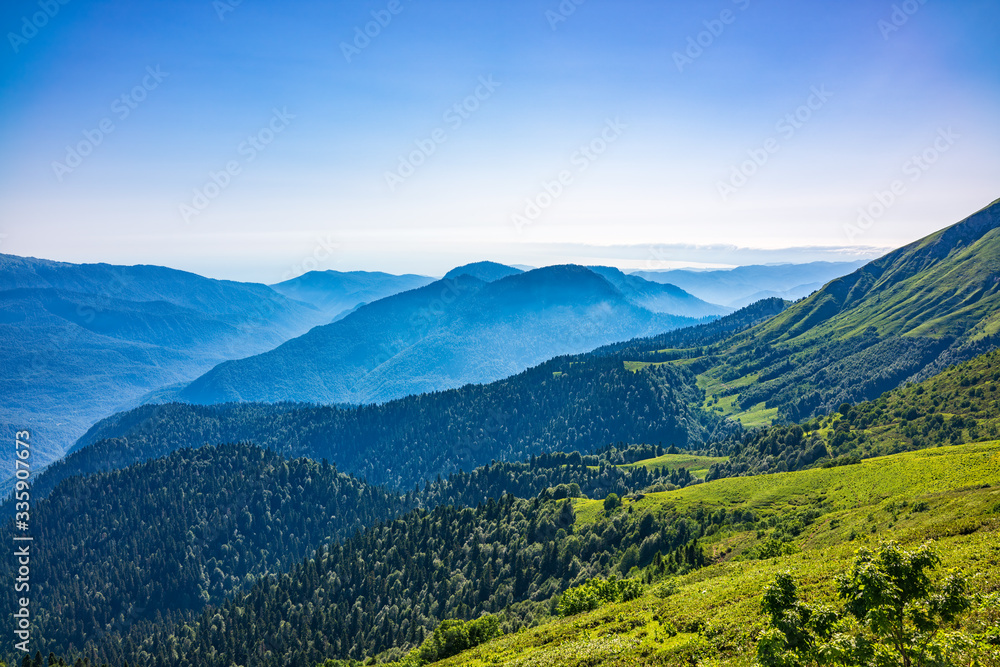 View over the Green Valley, surrounded by high mountains on a summer sunset. Layers of mountains in the haze during sunset. View over the Green Valley, surrounded by high mountains on a summer sunset. Layers of mountains in the haze during sunset.