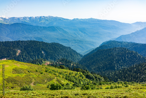 View over the Green Valley, surrounded by high mountains on a summer sunset. Layers of mountains in the haze during sunset.