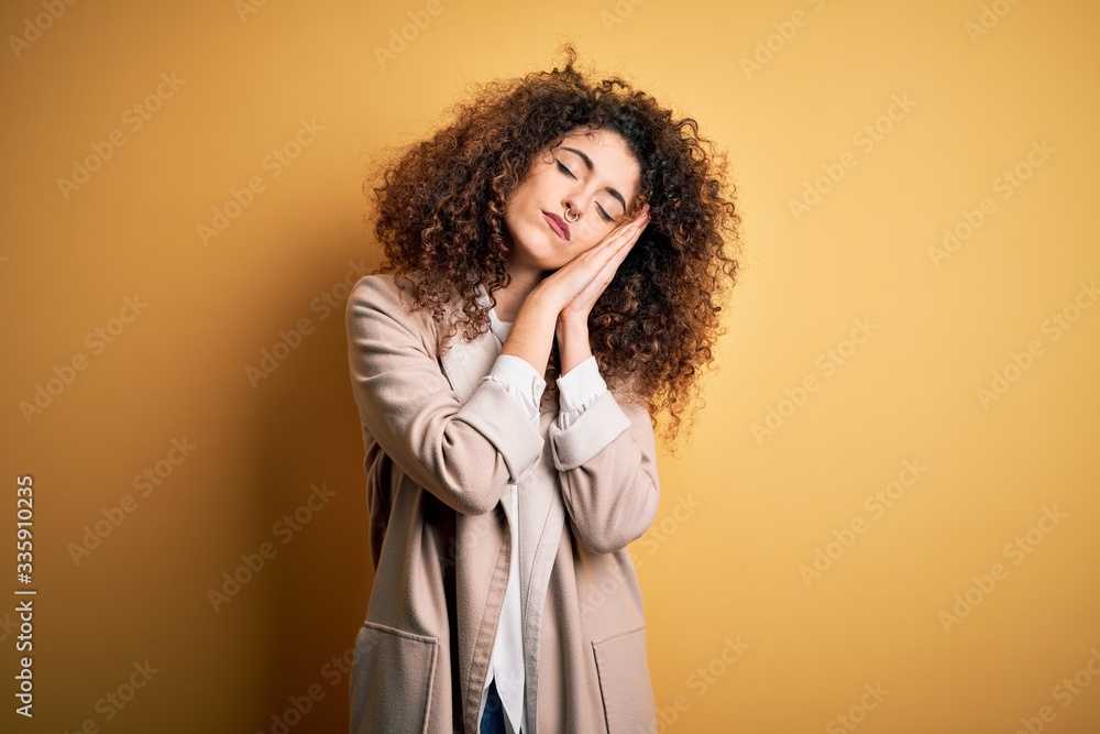 Young beautiful brunette woman with curly hair and piercing wearing casual t-shirt and diadem sleeping tired dreaming and posing with hands together while smiling with closed eyes. Young beautiful brunette woman with curly hair and piercing wearing casual t-shirt and diadem sleeping tired dreaming and posing with hands together while smiling with closed eyes.