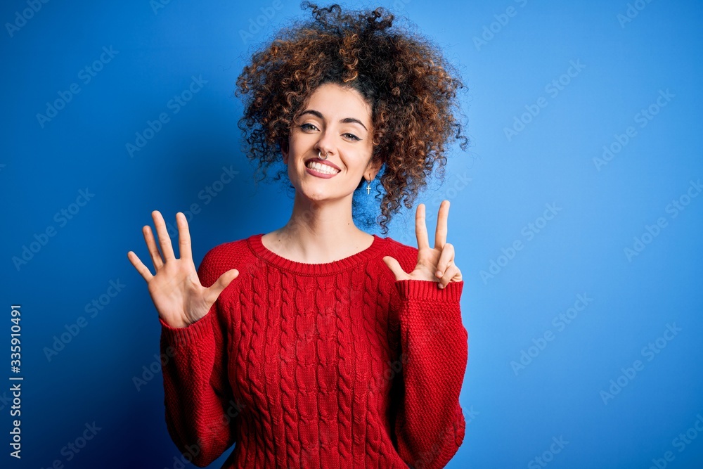 Young beautiful woman with curly hair and piercing wearing casual red sweater showing and pointing up with fingers number eight while smiling confident and happy. Young beautiful woman with curly hair and piercing wearing casual red sweater showing and pointing up with fingers number eight while smiling confident and happy.