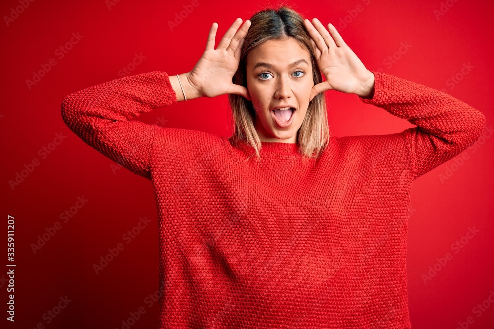 Young beautiful blonde woman wearing casual sweater over red isolated background Smiling cheerful playing peek a boo with hands showing face. Surprised and exited Young beautiful blonde woman wearing casual sweater over red isolated background Smiling cheerful playing peek a boo with hands showing face. Surprised and exited