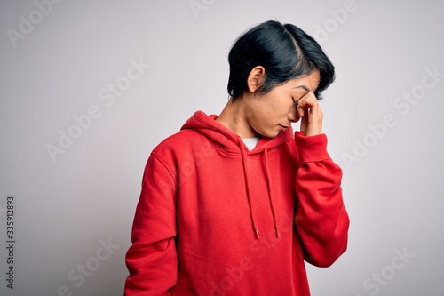 Young beautiful asian girl wearing casual sweatshirt with hoodie over white background tired rubbing nose and eyes feeling fatigue and headache. Stress and frustration concept. © Krakenimages.com