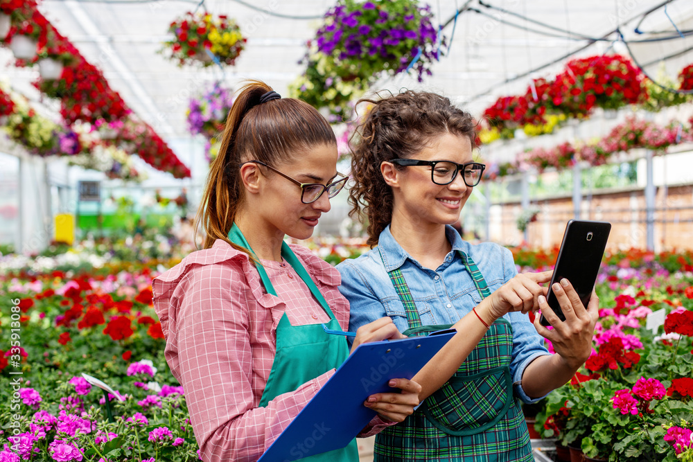 Two woman with notepad and tablet work in nursery garden with flowers Two woman with notepad and tablet work in nursery garden with flowers
