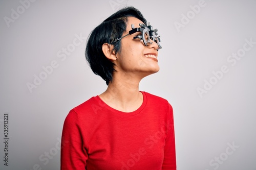 Young beautiful asian girl wearing optometry glasses standing over isolated white background looking away to side with smile on face, natural expression. Laughing confident.