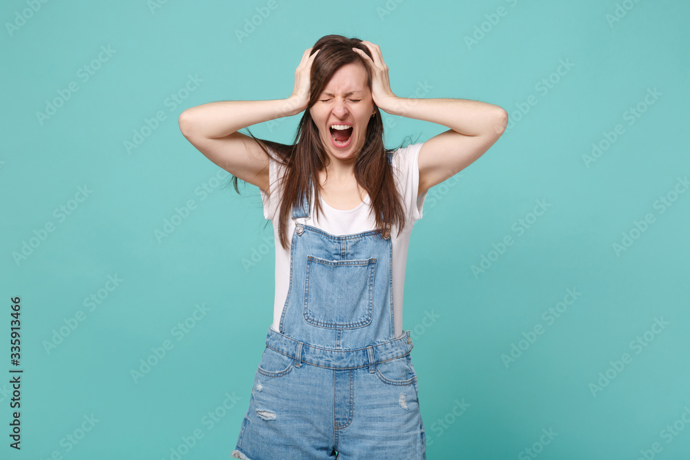Frustrated young brunette woman in casual denim clothes posing isolated on blue turquoise background. People lifestyle concept. Mock up copy space. Put hands on head, keeping eyes closed, screaming. Frustrated young brunette woman in casual denim clothes posing isolated on blue turquoise background. People lifestyle concept. Mock up copy space. Put hands on head, keeping eyes closed, screaming.