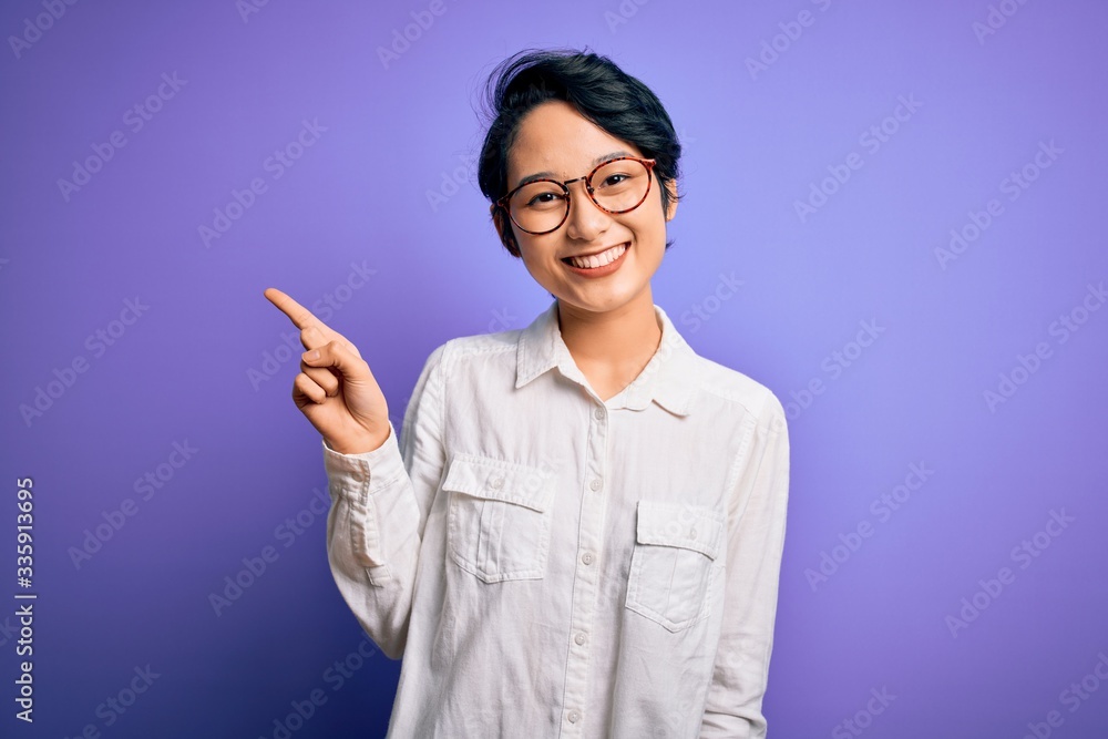 Young beautiful asian girl wearing casual shirt and glasses standing over purple background pointing finger up with successful idea. Exited and happy. Number one. Young beautiful asian girl wearing casual shirt and glasses standing over purple background pointing finger up with successful idea. Exited and happy. Number one.
