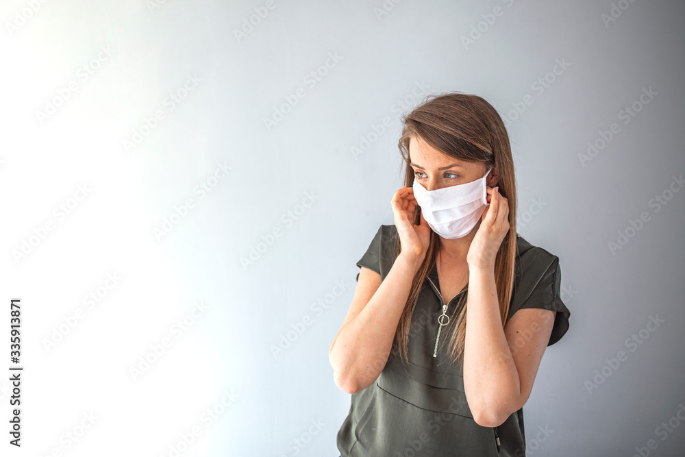 Beautiful caucasian young woman in t-shirt with disposable face mask. Protection versus viruses and infection. Studio portrait, concept with grey background. She is gesturing Beautiful caucasian young woman in t-shirt with disposable face mask. Protection versus viruses and infection. Studio portrait, concept with grey background. She is gesturing