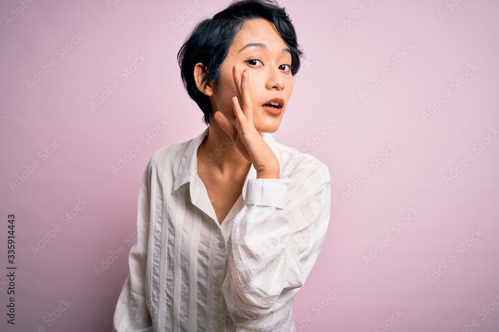 Young beautiful asian girl wearing casual shirt standing over isolated pink background hand on mouth telling secret rumor, whispering malicious talk conversation Young beautiful asian girl wearing casual shirt standing over isolated pink background hand on mouth telling secret rumor, whispering malicious talk conversation