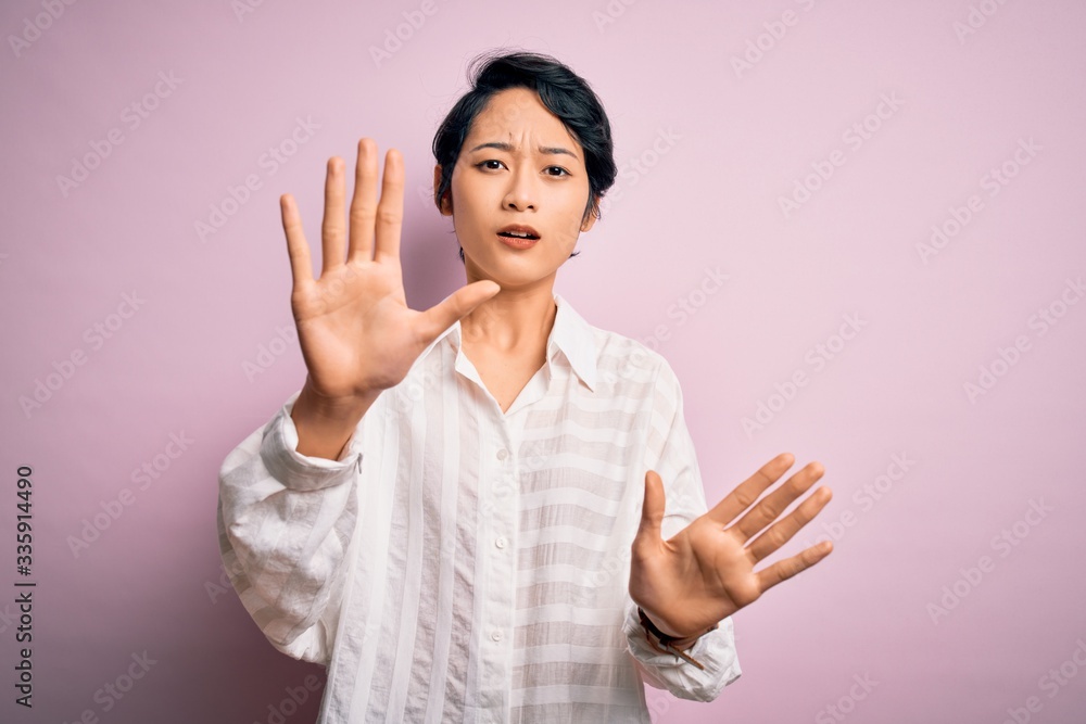 Young beautiful asian girl wearing casual shirt standing over isolated pink background doing stop gesture with hands palms, angry and frustration expression Young beautiful asian girl wearing casual shirt standing over isolated pink background doing stop gesture with hands palms, angry and frustration expression