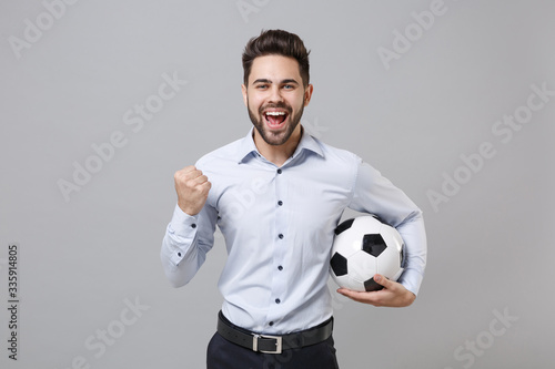 Happy young business man football fan in light shirt isolated on grey background. Achievement career wealth sport leisure concept. Cheer up support favorite team with soccer ball doing winner gesture.