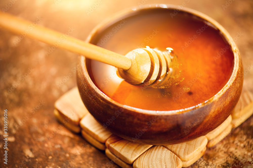 Honey dripping from honey dipper in wooden bowl. Close-up. Healthy organic Thick honey dipping from the wooden honey spoon, closeup. Top view Honey dripping from honey dipper in wooden bowl. Close-up. Healthy organic Thick honey dipping from the wooden honey spoon, closeup. Top view