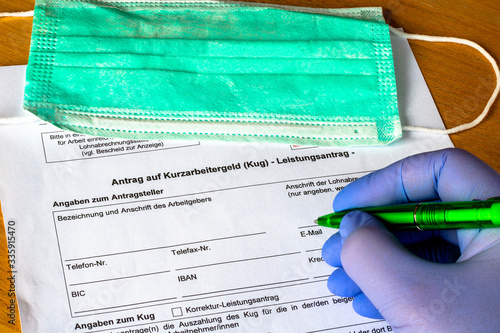 Antrag auf Kurzarbeitergeld wird von Person mit Schutzhandschuh ausgefüllt. Im Hintergrund liegt eine Atemschutzmaske. 