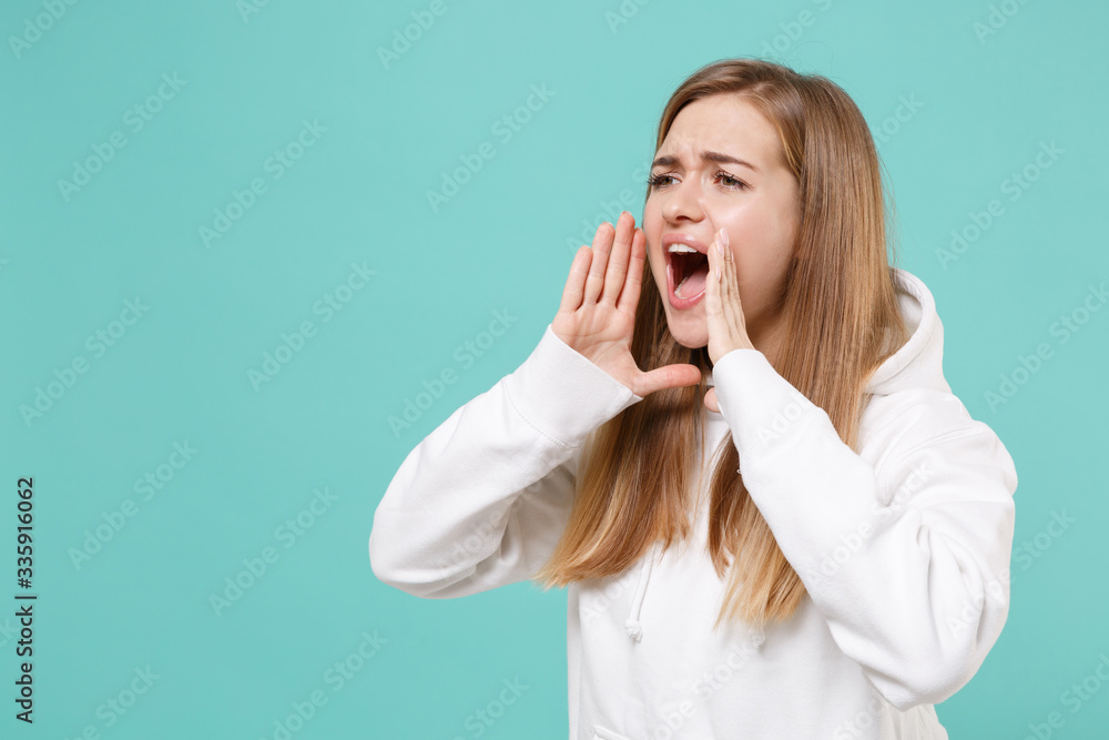 Worried young woman girl in casual white hoodie posing isolated on blue turquoise wall background. People lifestyle concept. Mock up copy space. Screaming with hands gesture near mouth, looking aside. Worried young woman girl in casual white hoodie posing isolated on blue turquoise wall background. People lifestyle concept. Mock up copy space. Screaming with hands gesture near mouth, looking aside.