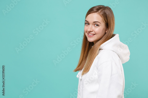 Side view of pretty young woman girl in casual white hoodie posing isolated on blue turquoise background studio portrait. People sincere emotions lifestyle concept. Mock up copy space. Looking camera.