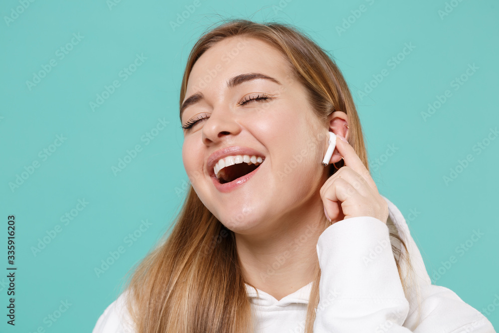 Funny young woman in casual white hoodie posing isolated on blue turquoise background studio portrait. People lifestyle concept. Mock up copy space. Listen music with air pods, keeping eyes closed. Funny young woman in casual white hoodie posing isolated on blue turquoise background studio portrait. People lifestyle concept. Mock up copy space. Listen music with air pods, keeping eyes closed.