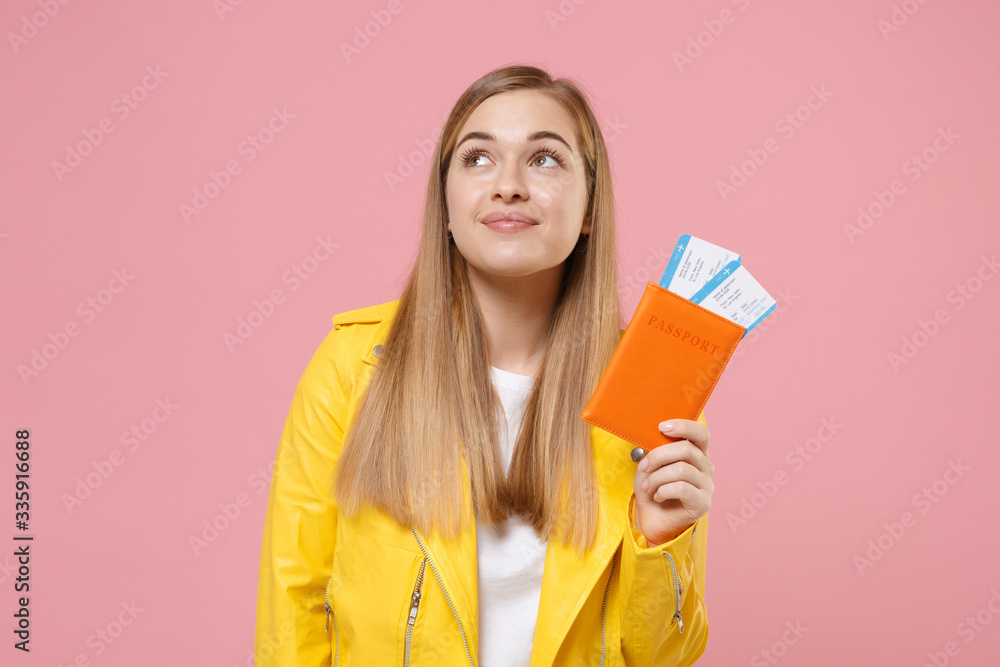 Pensive young woman girl in yellow leather jacket posing isolated on pastel pink wall background studio. People lifestyle concept. Mock up copy space. Hold passport tickets boarding pass, looking up. Pensive young woman girl in yellow leather jacket posing isolated on pastel pink wall background studio. People lifestyle concept. Mock up copy space. Hold passport tickets boarding pass, looking up.