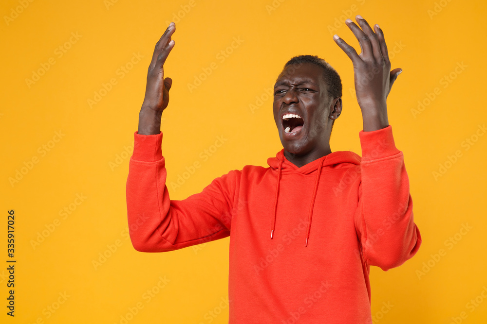 Angry irritated young african american man guy in red streetwear hoodie isolated on yellow background. People lifestyle concept. Mock up copy space. Screaming swearing, spreading hands, looking aside. Angry irritated young african american man guy in red streetwear hoodie isolated on yellow background. People lifestyle concept. Mock up copy space. Screaming swearing, spreading hands, looking aside.