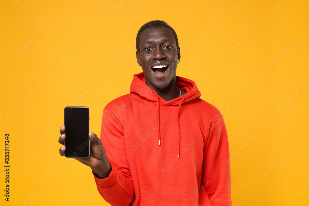 Excited young african american man guy in red streetwear hoodie posing isolated on yellow background in studio. People lifestyle concept. Mock up copy space. Hold mobile phone with blank empty screen. Excited young african american man guy in red streetwear hoodie posing isolated on yellow background in studio. People lifestyle concept. Mock up copy space. Hold mobile phone with blank empty screen.
