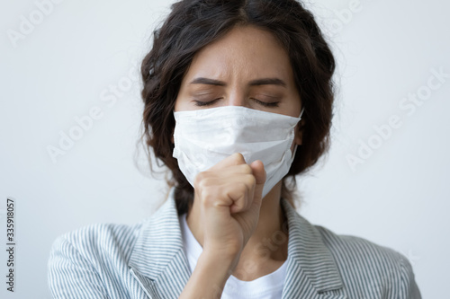 Head shot close up young unhealthy woman in facial medical facemask coughing, responsible for not spreading virus infection, isolated on blue studio background, flu grippe coronavirus quarantine. photo