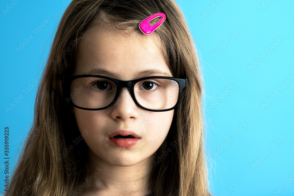 Close up portrait of a child school girl wearing looking glasses isolated on blue background.