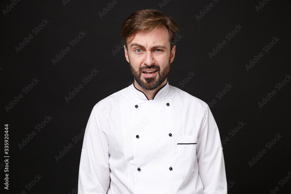 Confused perplexed young bearded male chef cook or baker man in white uniform shirt posing isolated on black wall background studio portrait. Cooking food concept. Mock up copy space. Looking camera. Confused perplexed young bearded male chef cook or baker man in white uniform shirt posing isolated on black wall background studio portrait. Cooking food concept. Mock up copy space. Looking camera.