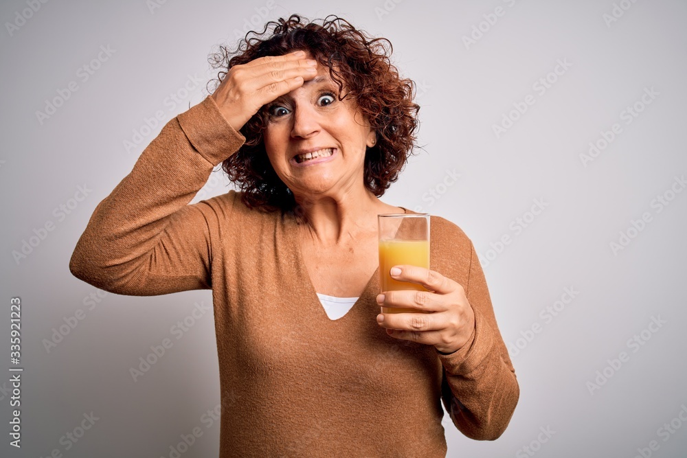 Middle age curly hair woman drinking healthy glass of orange juice over white background stressed with hand on head, shocked with shame and surprise face, angry and frustrated. Fear and upset Middle age curly hair woman drinking healthy glass of orange juice over white background stressed with hand on head, shocked with shame and surprise face, angry and frustrated. Fear and upset