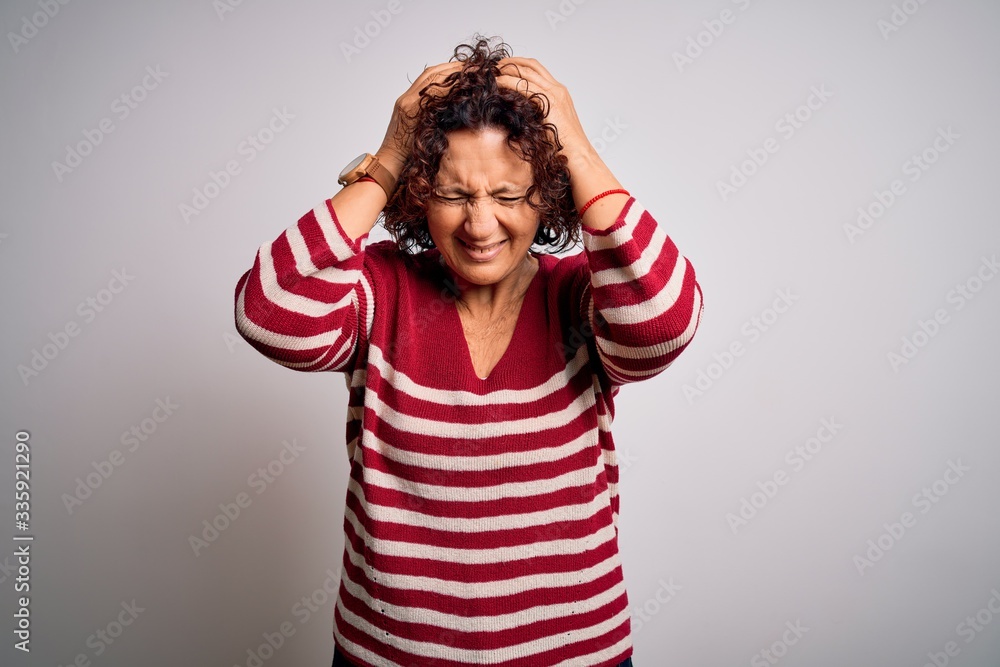 Middle age beautiful curly hair woman wearing casual striped sweater over white background suffering from headache desperate and stressed because pain and migraine. Hands on head. Middle age beautiful curly hair woman wearing casual striped sweater over white background suffering from headache desperate and stressed because pain and migraine. Hands on head.