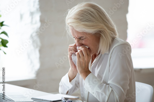 Vászonkép Unhappy 60 years old businesswoman sneeze close up, suffering from severe runny nose