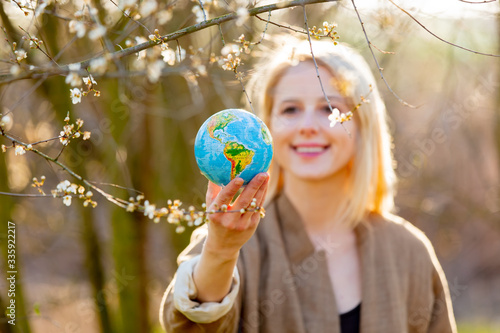 Blonde woman holds Earth globe in blooming cherry garden