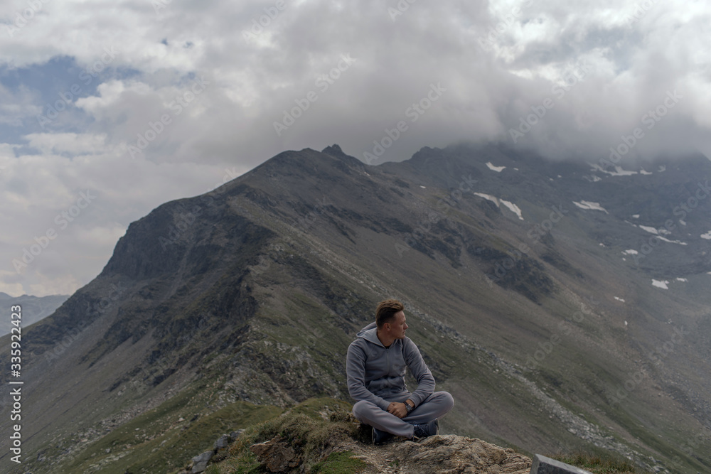 Fototapeta premium Young man meditates on the top of Alpine mountains.