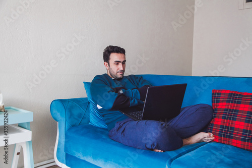 Brunette man sitting on the sofa in front of his laptop. Covid concept. Self-defense concept. 