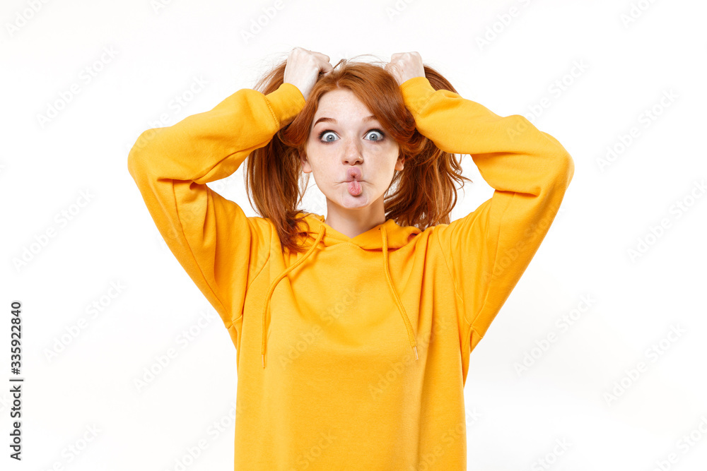 Funny young redhead woman girl in yellow hoodie posing isolated on white background. People lifestyle concept. Mock up copy space. Having fun holding hair like ponytails, making fish face with lips. Funny young redhead woman girl in yellow hoodie posing isolated on white background. People lifestyle concept. Mock up copy space. Having fun holding hair like ponytails, making fish face with lips.