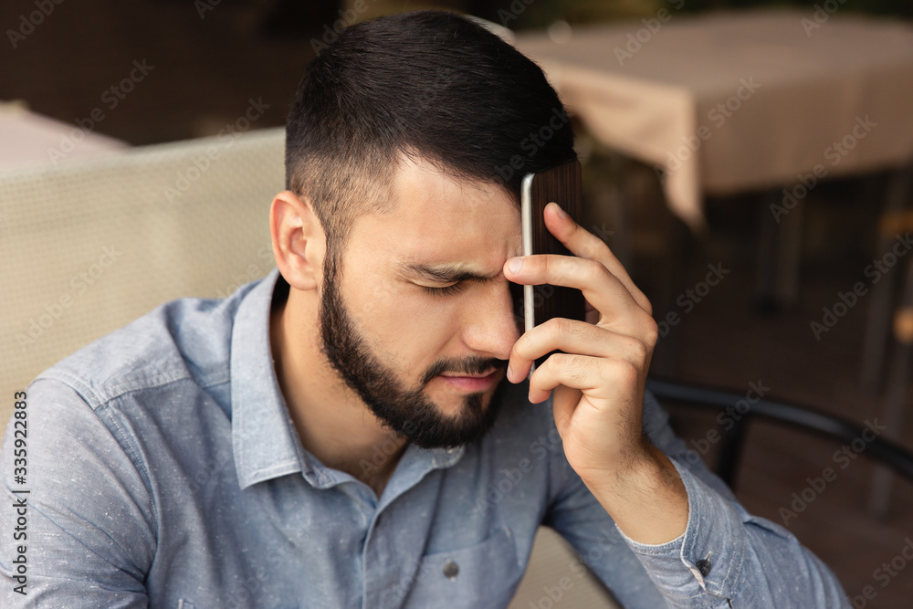 Unhappy man holding a phone near his head. Headache from hard work at home Unhappy man holding a phone near his head. Headache from hard work at home