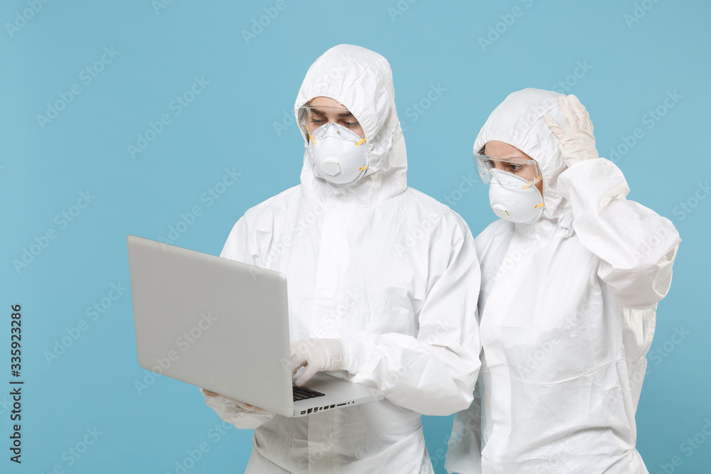 People in protective suits respirator masks hold work on laptop pc computer isolated on blue background studio. Epidemic pandemic new rapidly spreading coronavirus 2019-ncov medicine flu virus concept People in protective suits respirator masks hold work on laptop pc computer isolated on blue background studio. Epidemic pandemic new rapidly spreading coronavirus 2019-ncov medicine flu virus concept