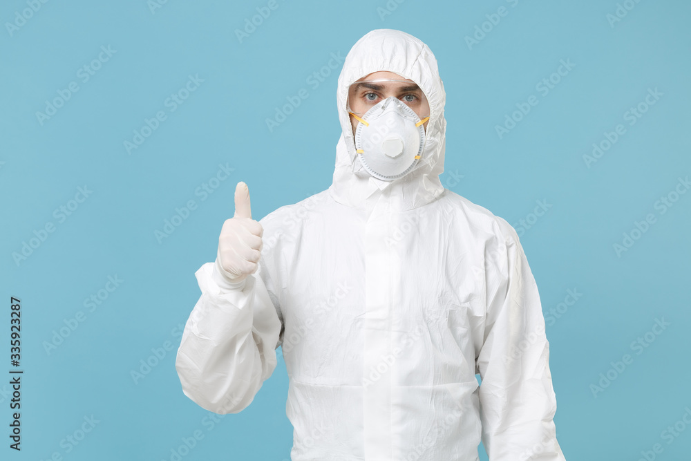 Man in white protective suit respirator mask isolated on blue background studio. Epidemic pandemic new rapidly spreading coronavirus 2019-ncov originating in Wuhan China, medicine flu virus concept. Man in white protective suit respirator mask isolated on blue background studio. Epidemic pandemic new rapidly spreading coronavirus 2019-ncov originating in Wuhan China, medicine flu virus concept.