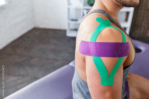 Kinesiology taping. Kinesiology tape on patient shoulder. Injured shoulder treatment of young male athlete. Post traumatic rehabilitation, sport physical therapy, recovery concept.