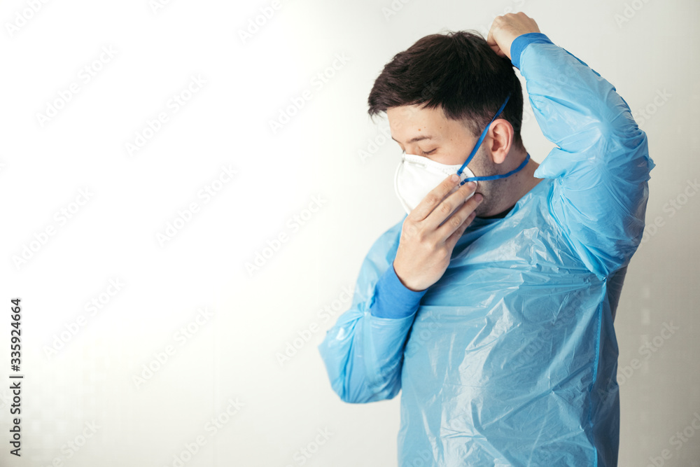 Young man with blue biohazard suit putting a mask with white background Young man with blue biohazard suit putting a mask with white background