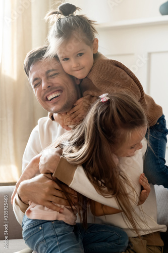 Vertical image playful little children embracing cuddling joyful father, welcoming at home. Happy young daddy enjoying sweet tender moment, glad to see small kids siblings. having fun together.