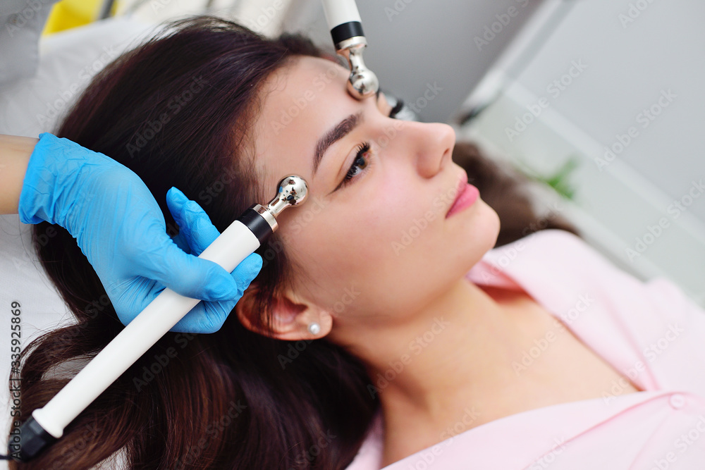 facial skin rejuvenation by microcurrent therapy in a modern cosmetology clinic. A cosmetologist uses a special device to perform a facial rejuvenation procedure for a pretty young girl.