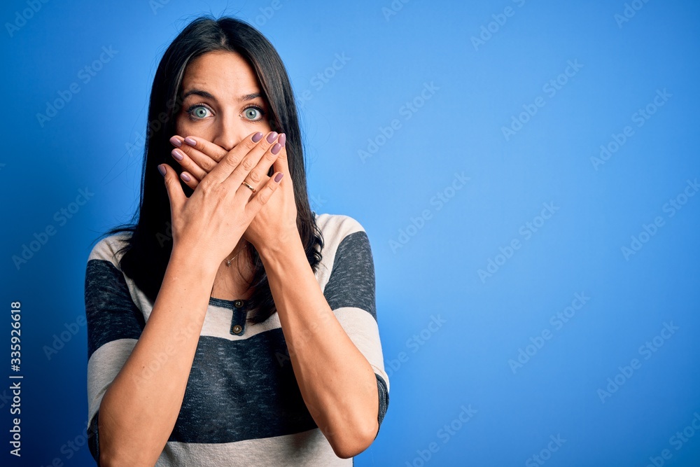 Young brunette woman with blue eyes wearing casual striped t-shirt standing over background shocked covering mouth with hands for mistake. Secret concept. Young brunette woman with blue eyes wearing casual striped t-shirt standing over background shocked covering mouth with hands for mistake. Secret concept.