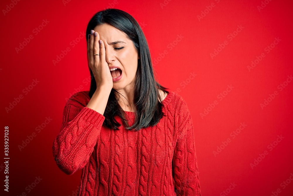 Young brunette woman with blue eyes wearing casual sweater over isolated red background Yawning tired covering half face, eye and mouth with hand. Face hurts in pain. Young brunette woman with blue eyes wearing casual sweater over isolated red background Yawning tired covering half face, eye and mouth with hand. Face hurts in pain.