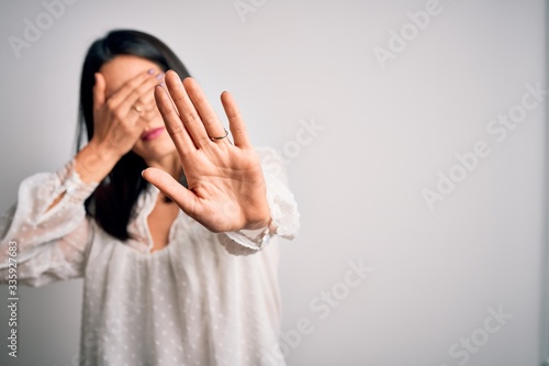 Young brunette woman with blue eyes wearing casual t-shirt over isolated white background covering eyes with hands and doing stop gesture with sad and fear expression. Embarrassed and negative