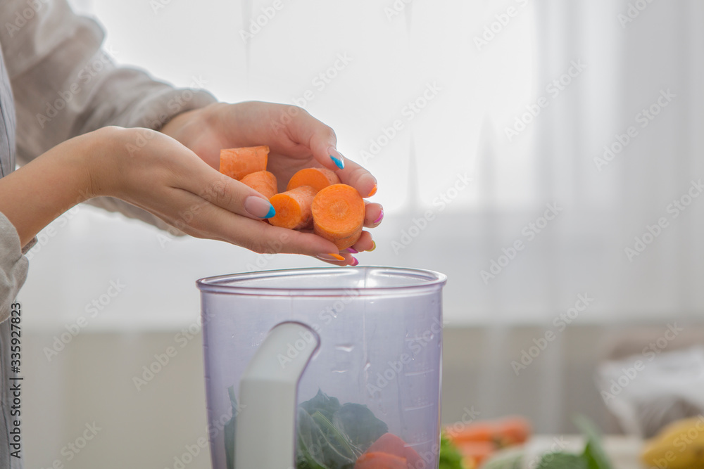 Woman blending carrot and other vegetables to make a healthy smoothie - obrazy, fototapety, plakaty 