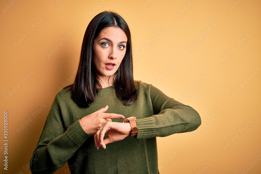 Young brunette woman with blue eyes wearing green casual sweater over yellow background In hurry pointing to watch time, impatience, upset and angry for deadline delay Young brunette woman with blue eyes wearing green casual sweater over yellow background In hurry pointing to watch time, impatience, upset and angry for deadline delay