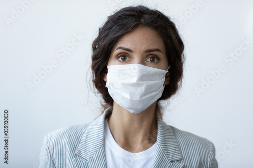 Head shot portrait of worrying young brunette woman covering nose and mouth with respiratory protective medical equipment. Stressed lady wearing facial mask, stop virus contagion, healthcare concept.