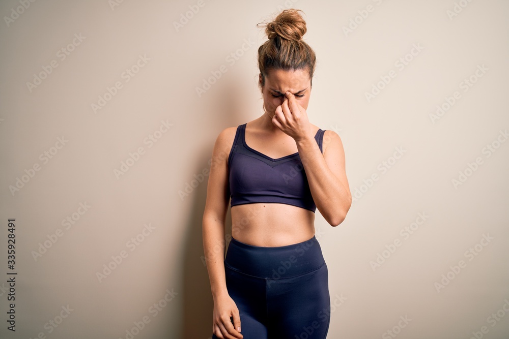 Young beautiful blonde sportswoman doing sport wearing sportswear over white background tired rubbing nose and eyes feeling fatigue and headache. Stress and frustration concept. Young beautiful blonde sportswoman doing sport wearing sportswear over white background tired rubbing nose and eyes feeling fatigue and headache. Stress and frustration concept.