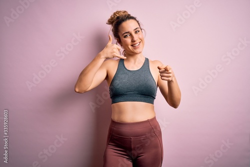 Young beautiful blonde sportswoman doing sport wearing sportswear over pink background smiling doing talking on the telephone gesture and pointing to you. Call me. © Krakenimages.com
